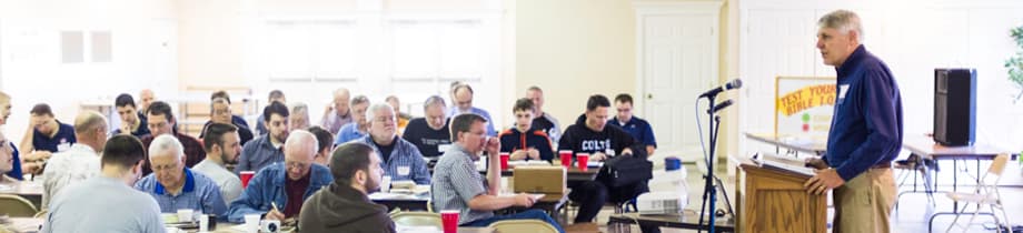 A speaker addressing men gathered around tables at the study